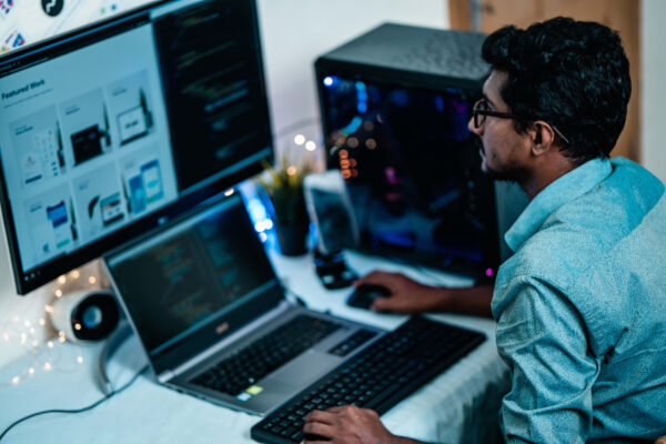 A man working at a desk with dual monitors and a keyboard, focused on his tasks.